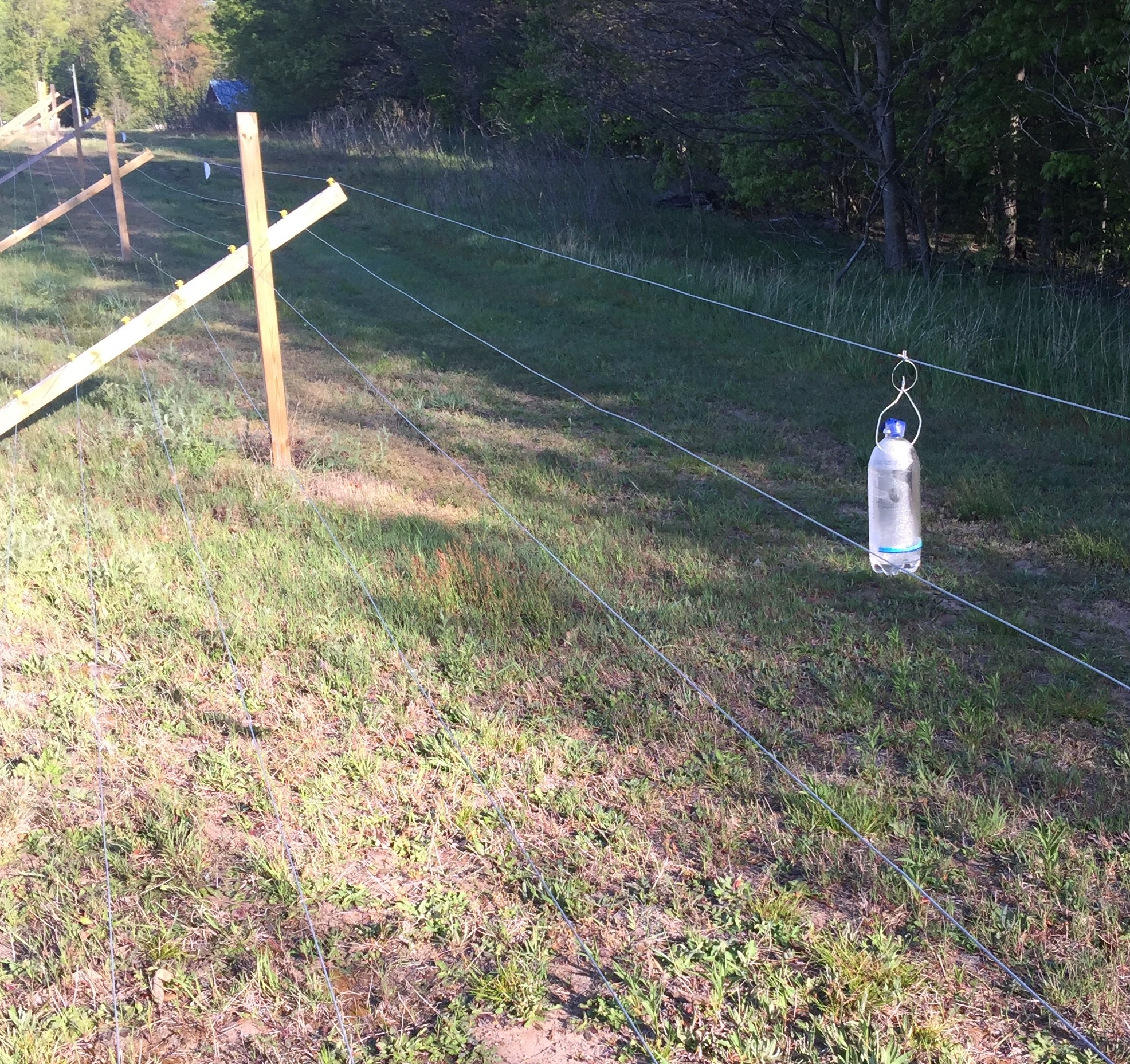 Plastic bottle filled with vodka hanging from a wire fence.